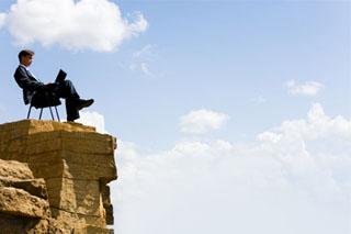 Businessman sitting on a chair at the top of a precipitous ledge.